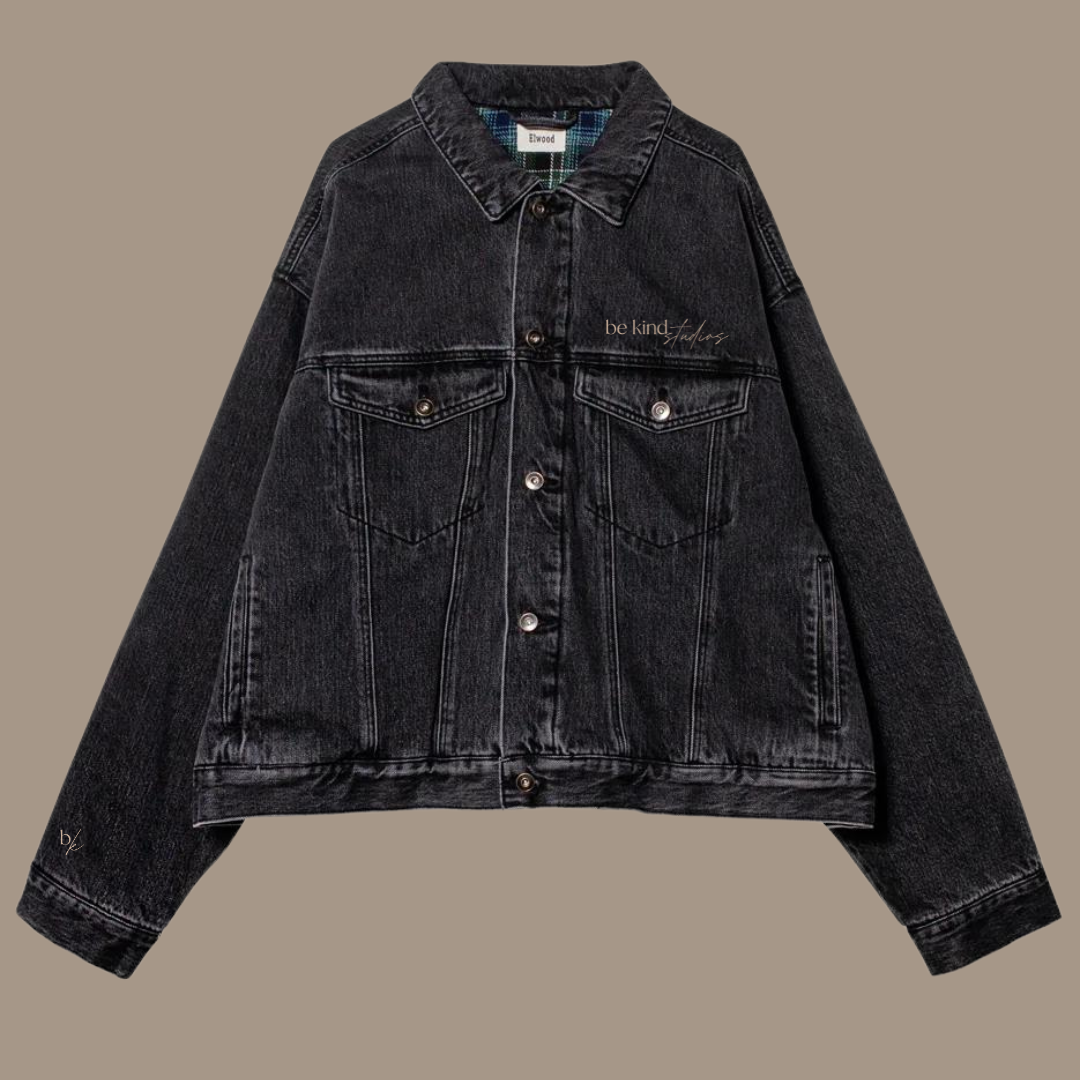 Button down black jean jacket with the words "be kind studios" embroidered on the front.