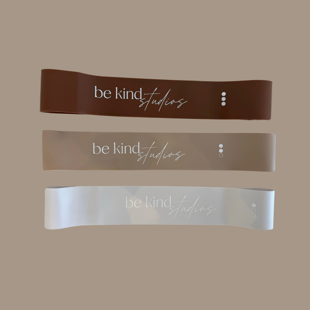Rubber booty bands, brown, beige, and white. Printed on them are the words "be kind studios"