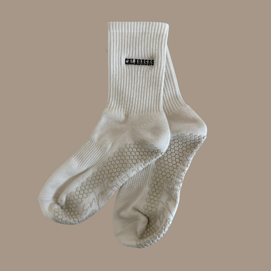 Beige grip socks with the word "CALABASAS" embroidered on the side horizontally & "be kind studios" embroidered on the bottom